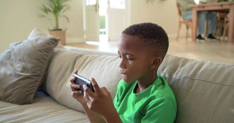 African american boy playing mobile game on sofa at home modern living room cozy open-plan interior