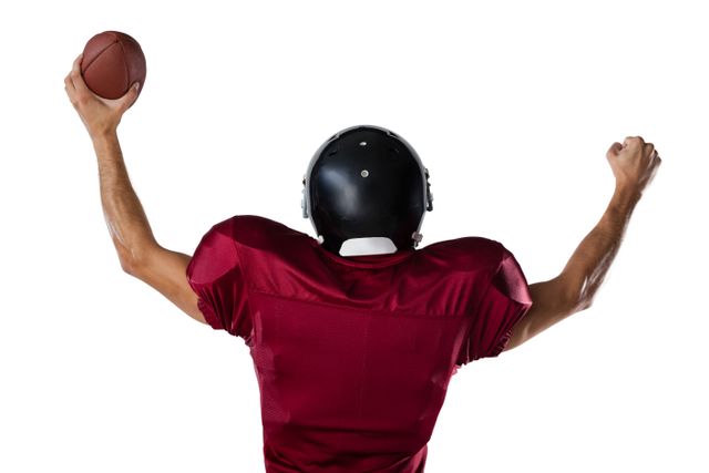 Rear view of sportsman holding football while standing with arms raised against white background