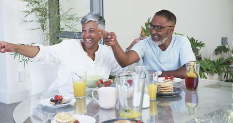 Smiling Couple Sharing Laughter Over Breakfast Table Indoors