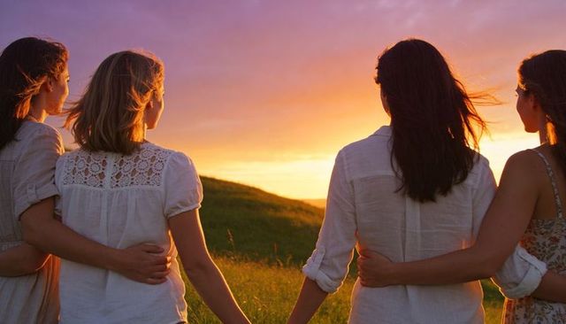 Four women linking arms on sunlit hill at sunset embracing friendship and unity