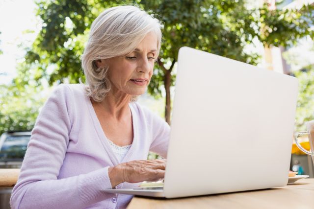 Senior woman using laptop in outdoor cafÃ© on a sunny day