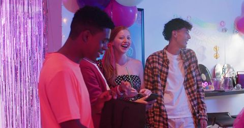 Friends celebrating at house party opening gift with colorful balloons and metallic fringe