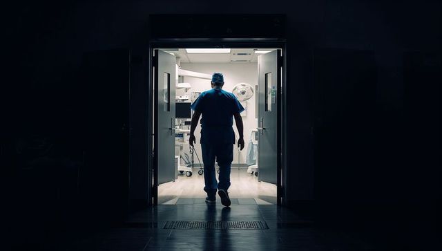 Surgeon walking into operating room through double doors backlit silhouette hospital corridor