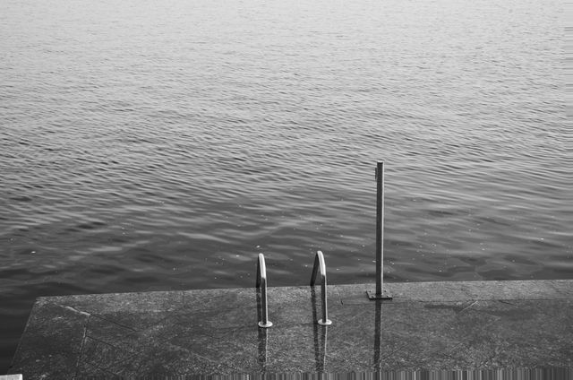 Monochrome photo capturing a minimalistic view of a calm ocean from a stone dock. Featuring simple lines and subdued tones, this photo emphasizes peace and simplicity. Ideal for use in interior design, wall art, meditation materials, or as a serene background in digital projects.