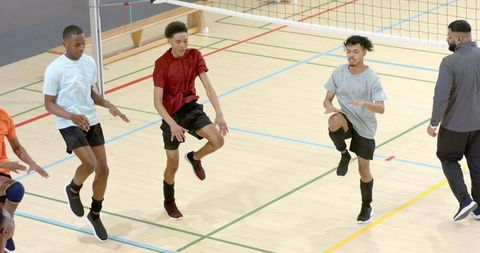 Youth male volleyball team performing single-leg hop warmup on indoor court with coach