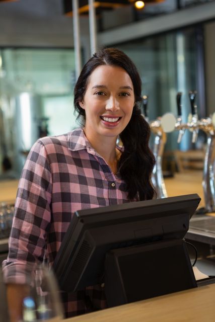 Portrait of smiling female owner using cash register at restaurant