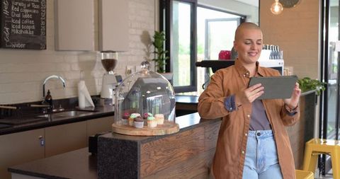 Barista using tablet at cafe counter with cupcake dome, espresso grinder and cozy interior