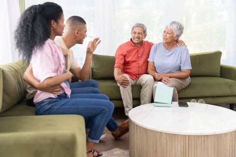 Young couple visiting older parents, sharing warm conversation on green sectional sofa