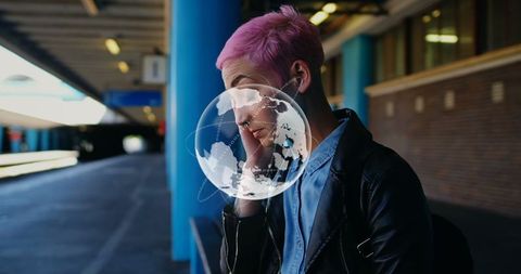 Tech saavy pink-haired woman at train station with digital globe overlay