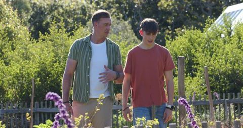 Parent and teen walking through sunlit community garden, talking by wooden picket fence