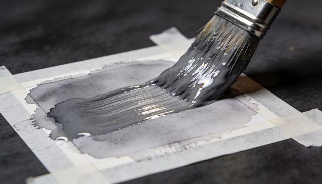 Closeup applying gray-black wash with flat brush on taped watercolor paper