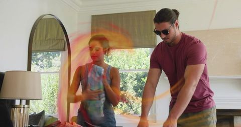 Young couple folding laundry together in sunlit living room sharing household chores