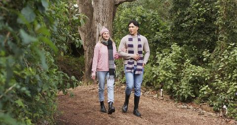Diverse couple walking arm-in-arm on woodland path wearing scarves and boots