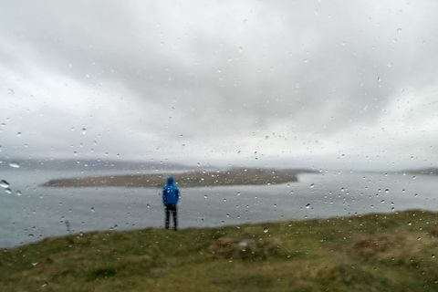 Person in Blue Raincoat Looking at Ocean on Overcast Day
