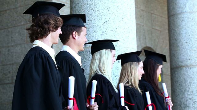 This image depicts a group of graduates wearing caps and gowns, standing proudly side by side as they hold their diplomas. Perfect for illustrating aspects of educational achievement, or promoting university and college graduation events or materials.