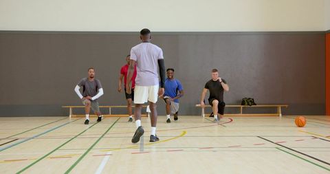 Coach leading diverse basketball team performing warmup lunges in indoor gymnasium