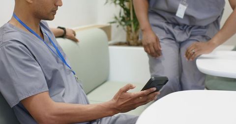 African american healthcare workers sitting in lounge checking smartphone during break