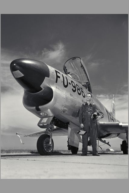 This black and white 1950s image captures a NACA test pilot standing proudly in front of an F-100 Super Sabre jet with a clear sky as backdrop. Useful for historical presentations, aviation articles, and military history documentation.