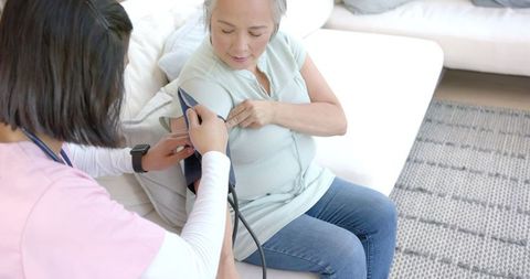 Home nursing care for senior woman by nurse monitoring blood pressure