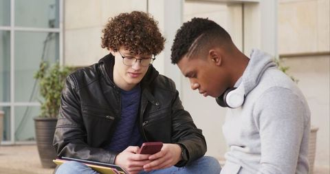 Multiracial college students collaborating and viewing smartphone together on campus steps
