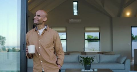 Middle-aged man enjoying coffee by sliding glass door in modern minimalist living room