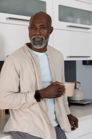 Mature african american man holding mug and glancing in minimalist contemporary kitchen