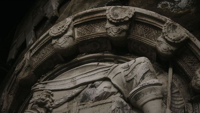 Weathered stone relief in arched niche with draped robes, rosettes and architectural detail