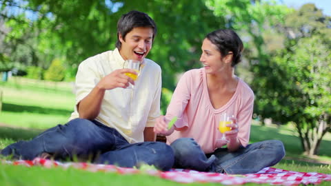 Happy Couple Enjoying Picnic with Orange Juice in Park