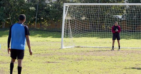 Players practicing penalty kick on soccer field in park