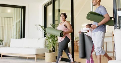 Diverse family carrying yoga mats toward sunlit patio for outdoor home workout
