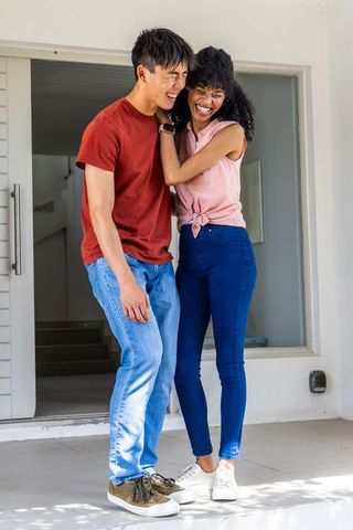 Laughing interracial couple celebrating new home on front porch wearing casual denim