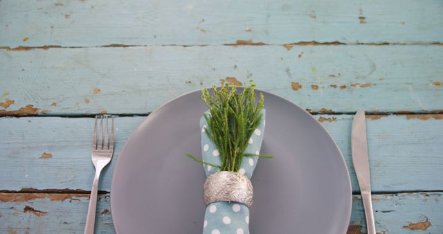 A gray plate with a decorative plant and silverware is set against a rustic blue wooden background, with copy space. The setting suggests a simple yet elegant dining arrangement, for a special occasion or a themed event.