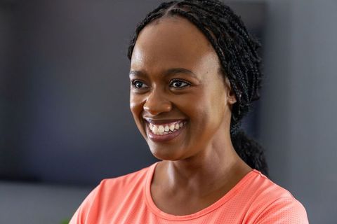 Confident black woman smiling in coral activewear, braided hair, indoor lifestyle portrait
