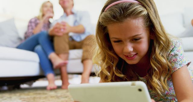 Happy Girl Playing with Tablet While Parents Relaxing in Background - Download Free Stock Images Pikwizard.com