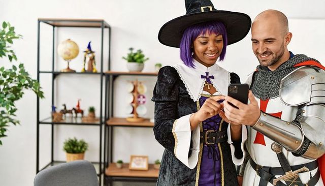 Smiling witch and knight checking smartphone in modern living room cosplay fantasy scene