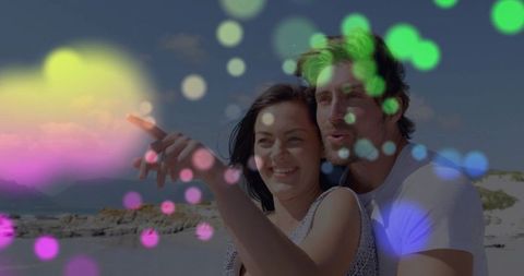 Couple pointing and gazing at horizon on rocky beach with colorful bokeh overlay