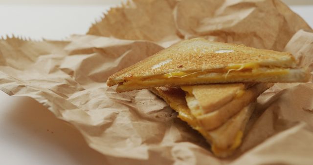 Stacked, golden-brown grilled cheese sandwiches wrapped in crumpled brown paper. Might be used for food blogs, sandwich shop advertisements, recipe illustrations, or promoting lunch meal options.