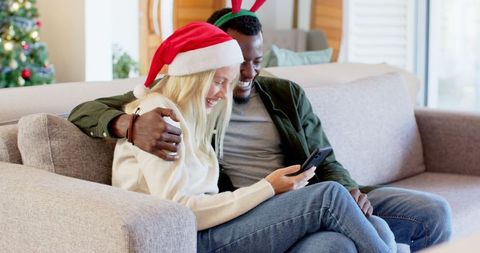 Interracial Couple Enjoying Christmas Moments With Smartphone on Sofa