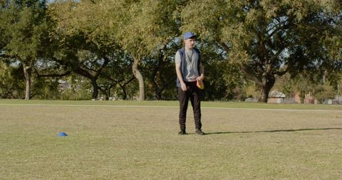 Young man holding yellow disc standing in park field preparing to throw frisbee
