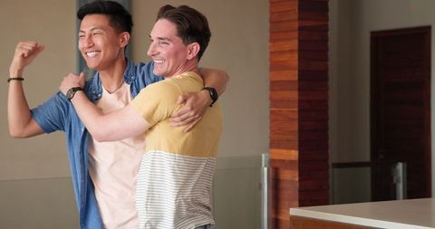 Joyful Diverse Male Couple Embracing in Celebration at Home