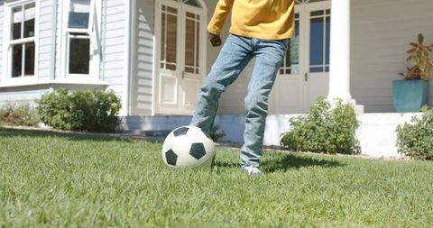 Boy practicing soccer on front lawn kicking ball near porch sunny home childhood activity