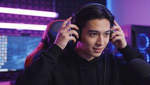 Young gamer adjusting over-ear headset at rgb streaming desk, focusing on gameplay