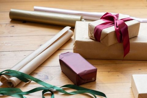 Rustic kraft-wrapped gift stack with red satin ribbon and wrapping rolls on wooden table