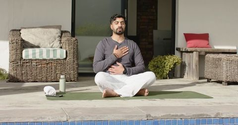 Indian man meditating poolside on green yoga mat practicing mindful breathing and wellness