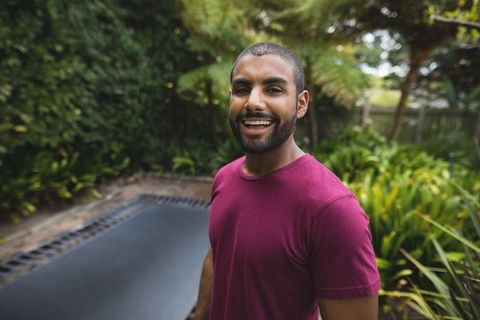 Smiling Man Standing Beside Trampoline in Sunny Backyard Garden