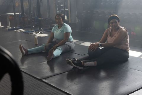 Two african american women stretching with medicine balls on gym mats showing strength and focus