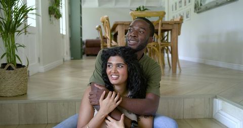 Multicultural couple embracing on home step in bright open-plan living interior