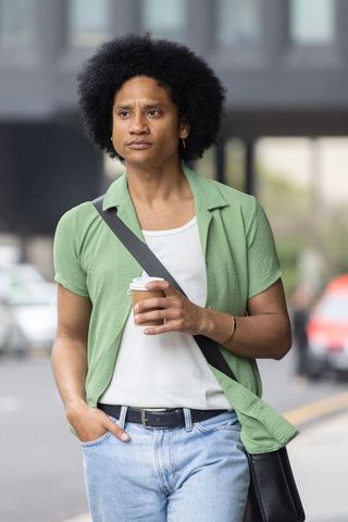 African man walking with takeaway coffee and crossbody bag in casual urban streetwear
