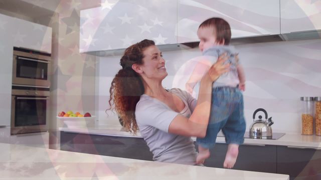 A cheerful mother lifting her baby in a contemporary kitchen with the USA flag overlaying the scene. Suitable for use in family, parenting, patriotic, lifestyle, and home-related projects. Ideal for advertisements, blog visuals, and promotional materials celebrating families and national pride.