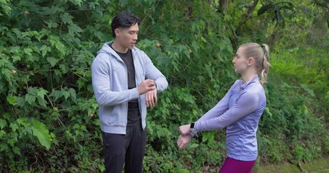 Couple checking smartwatches on woodland trail during outdoor workout routine